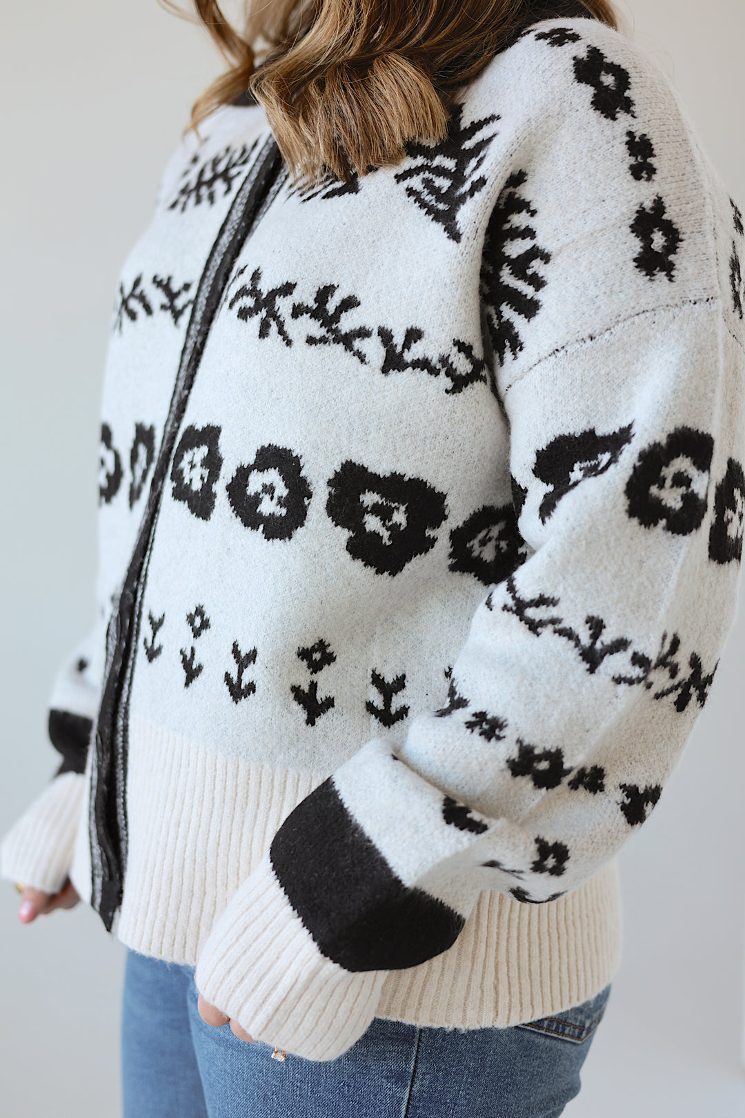 Person wearing a cream-colored sweater with black floral patterns on a plain background