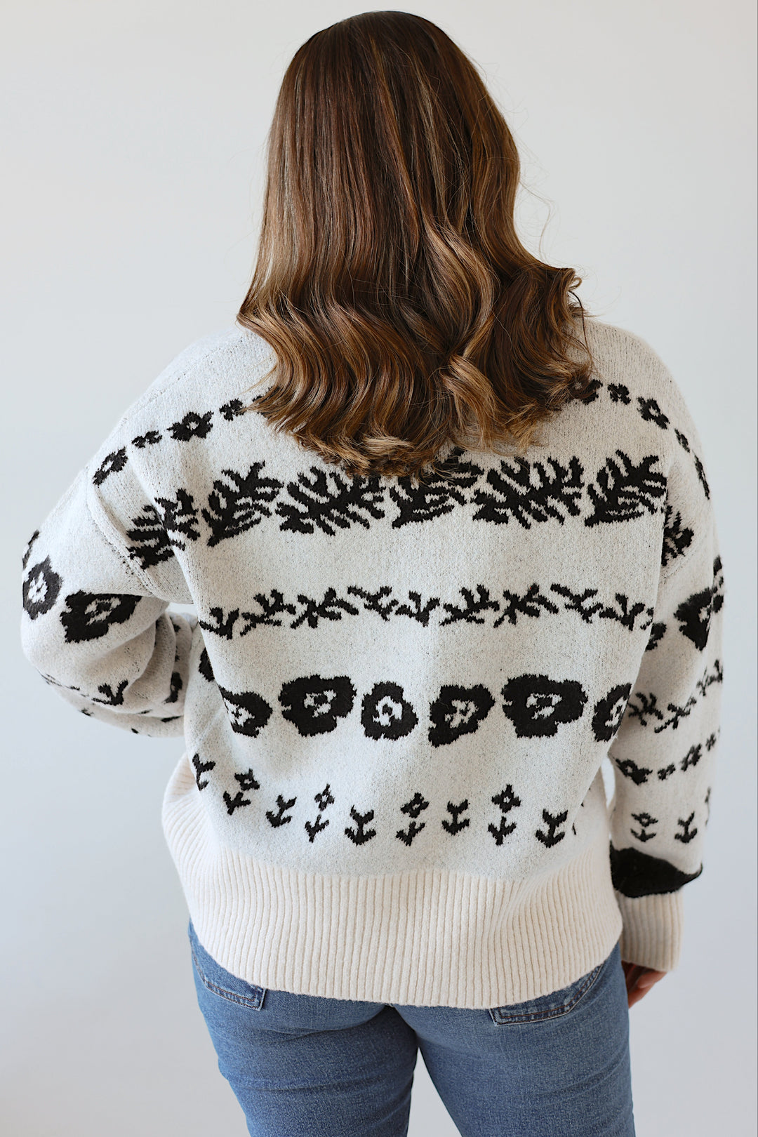 Person wearing a white sweater with black floral patterns against a plain background