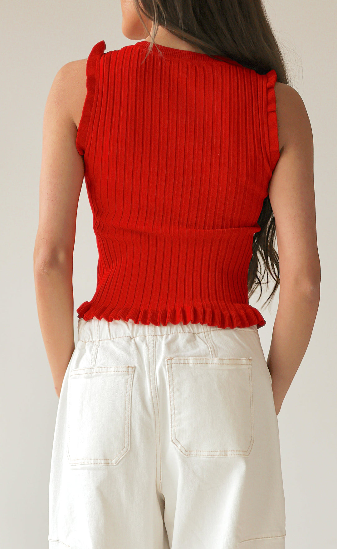 Person wearing a red sleeveless top and white pants on a plain background