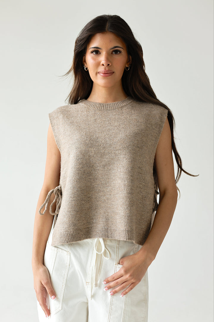 Woman wearing a beige sweater over white pants on a plain background