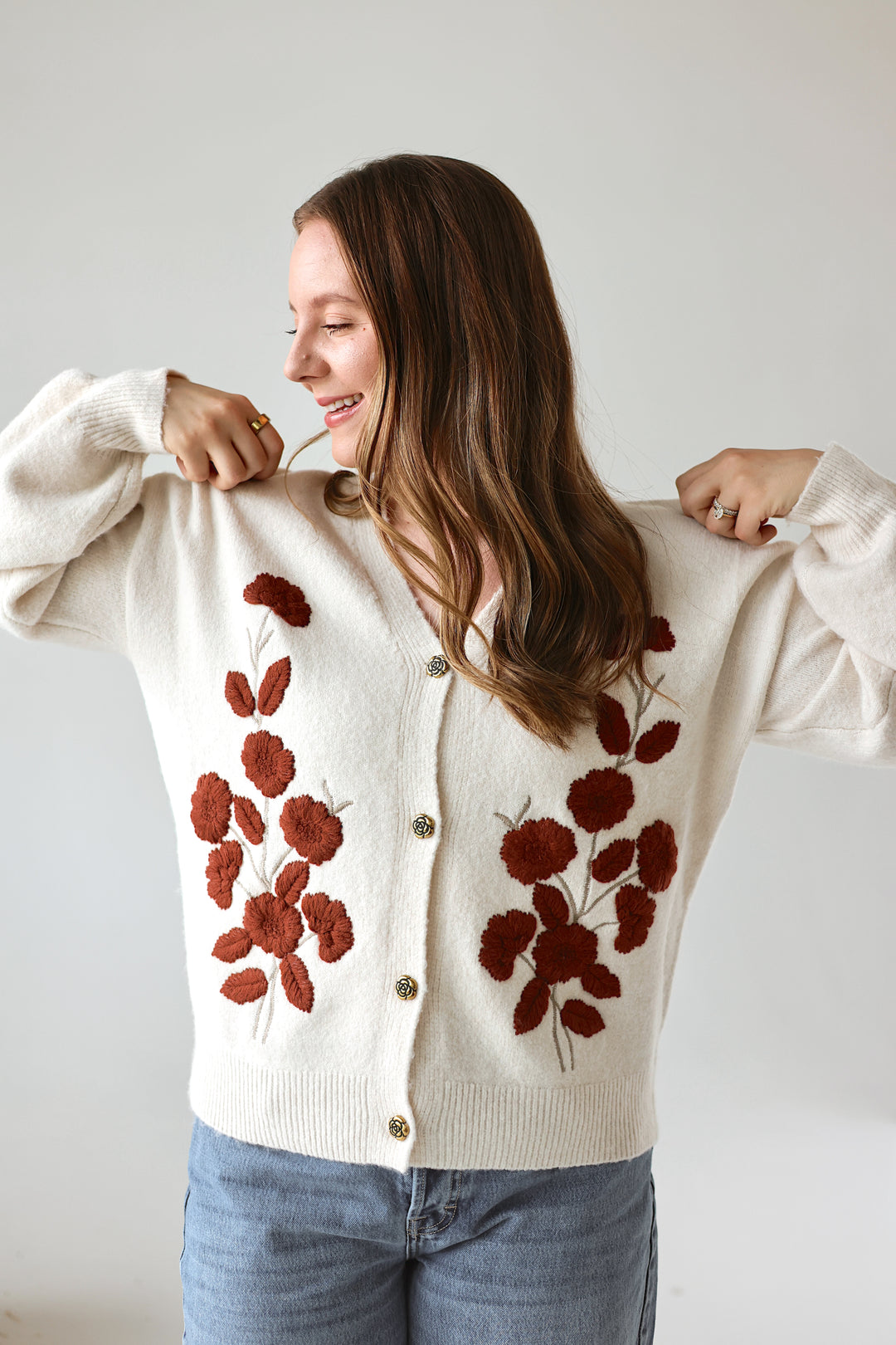 Model wearing the Rosalie floral embroidered cardigan in ivory with rust floral details in a studio background. 