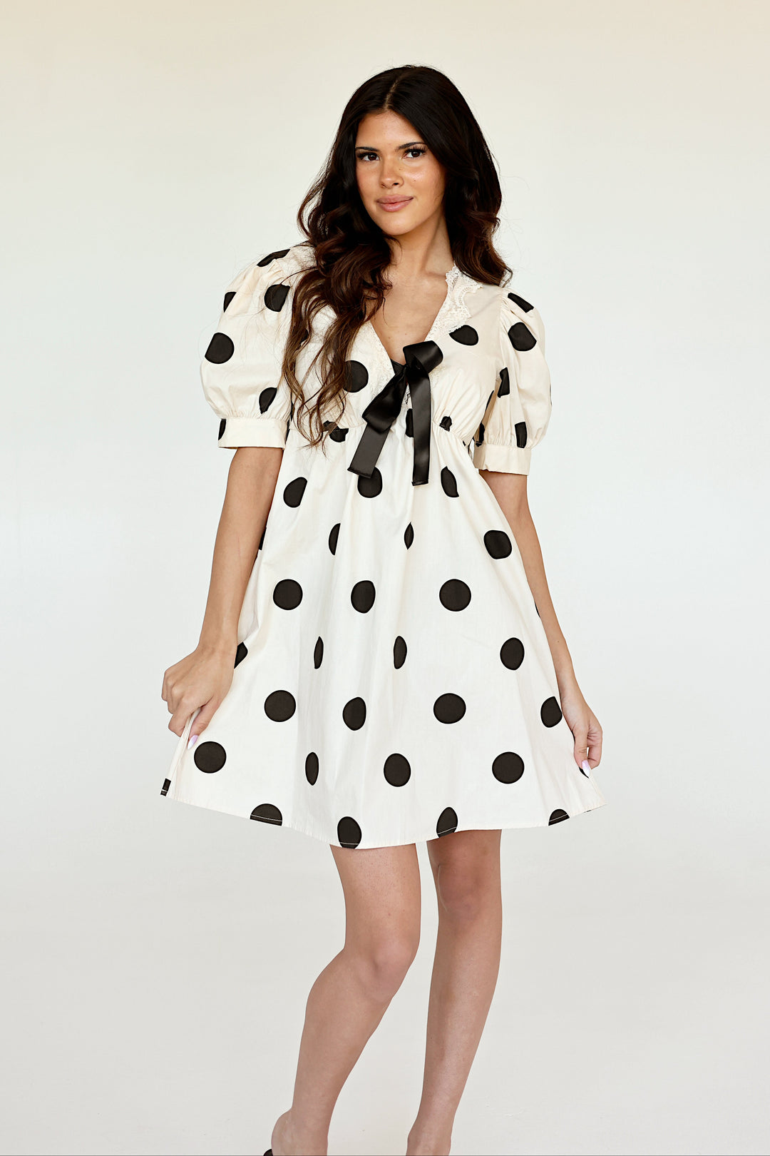 Model wearing the Colette ivory polka dot mini dress with puff sleeves and bow detail