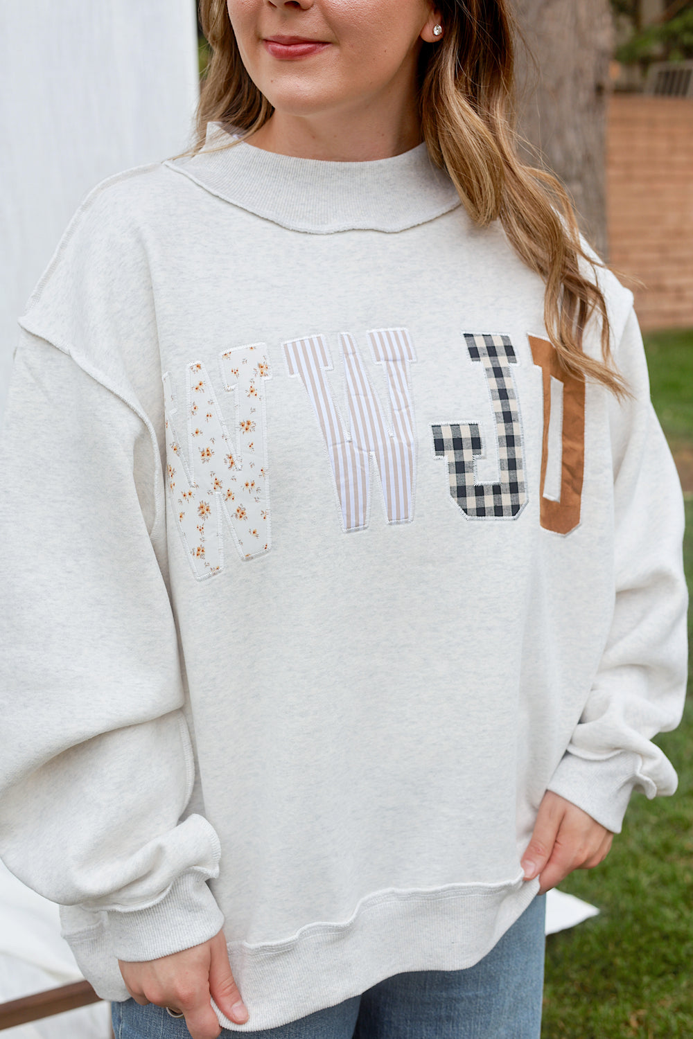 Close-up front view of the ash grey WWJD embroidered mockneck sweatshirt showing the mixed-fabric lettering.