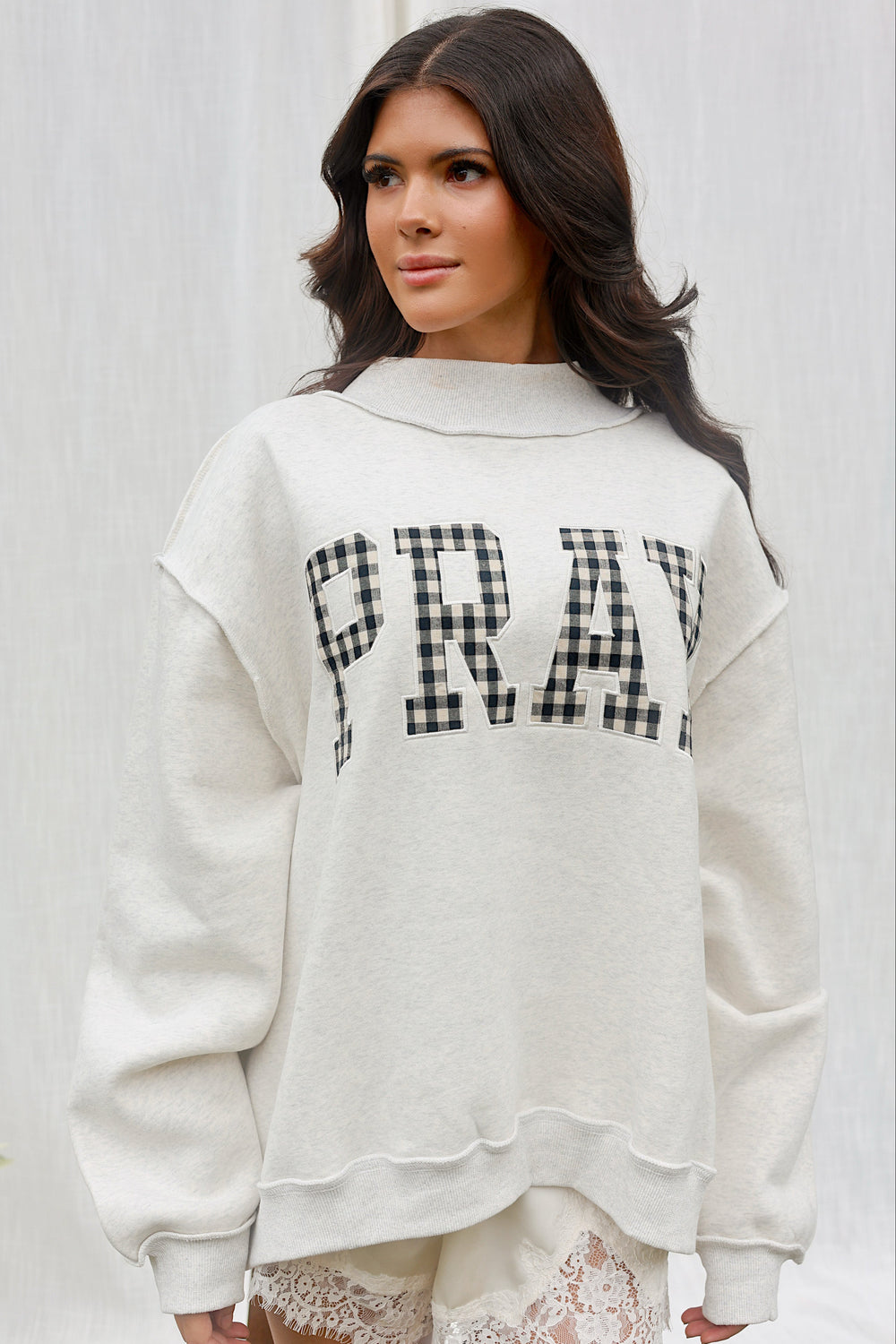 Front view of model wearing the PRAY gingham appliqué mockneck sweatshirt with lace shorts.