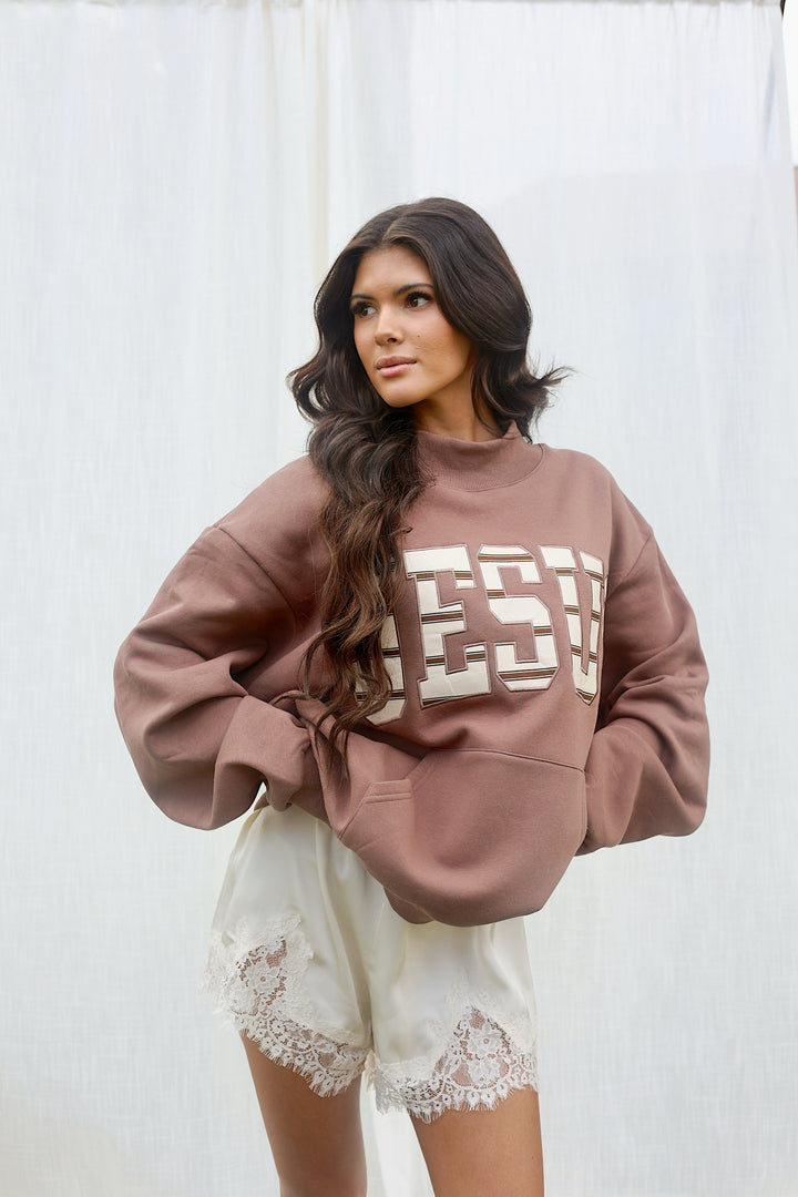 A woman wearing an oversized dusty rose sweatshirt with large cream block lettering that reads &